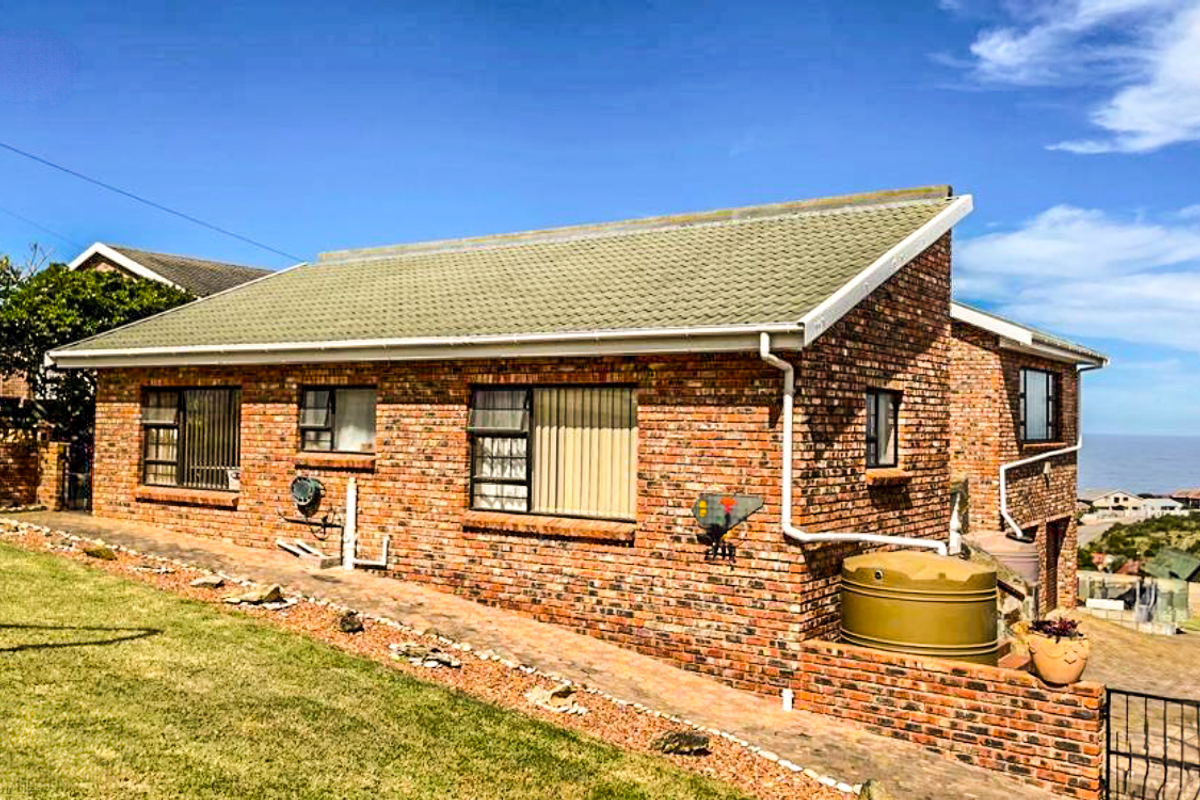 Rear view of a face brick house featuring a tiled roof, rainwater tank, and paved walkway with coastal views in the background.
