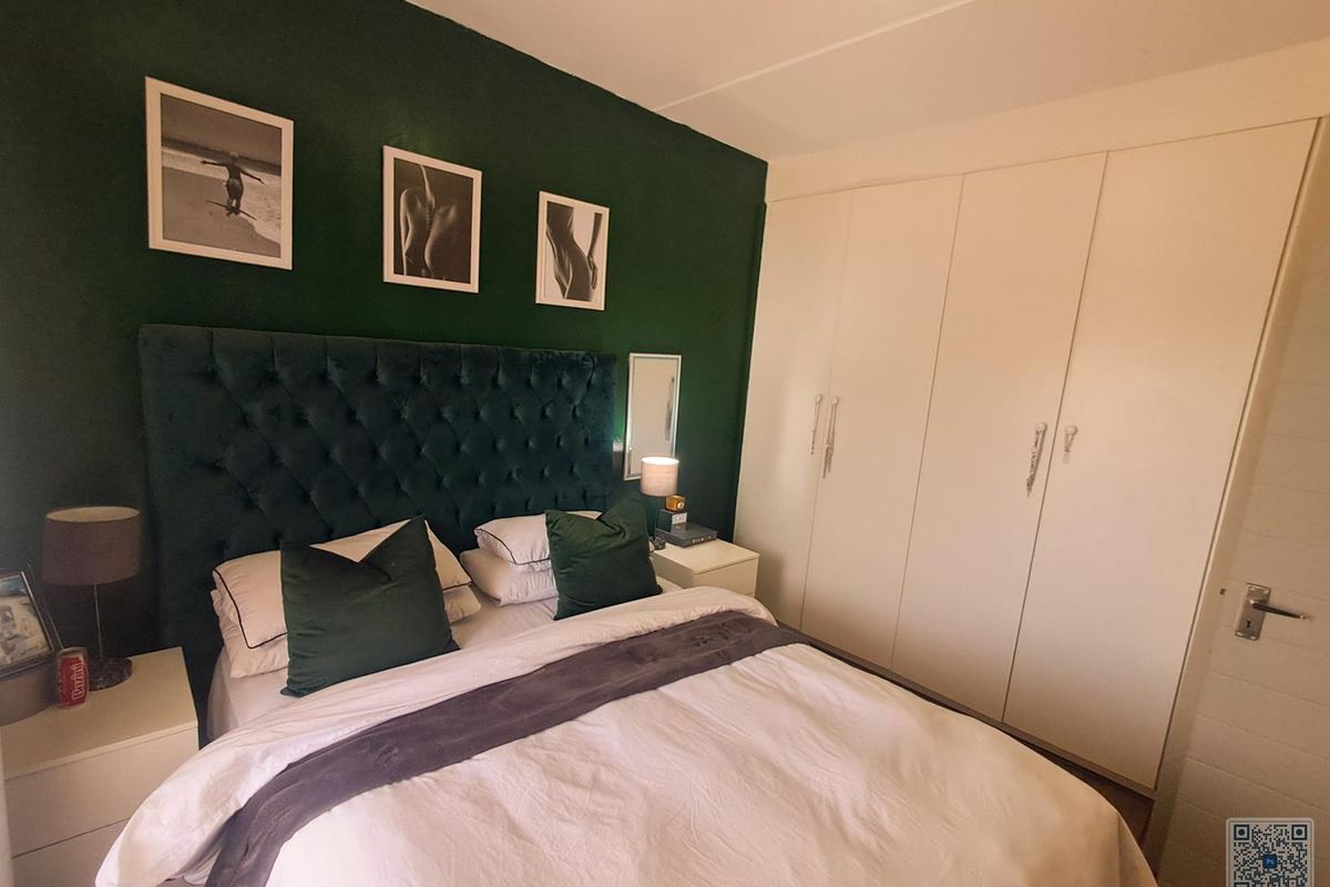 A well-maintained bedroom featuring a dark green accent wall, built-in white wardrobes, and neutral flooring.
