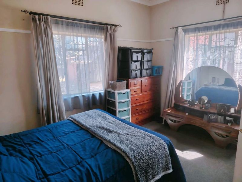A bedroom featuring natural light through two windows with security bars and classic picture rail detailing.