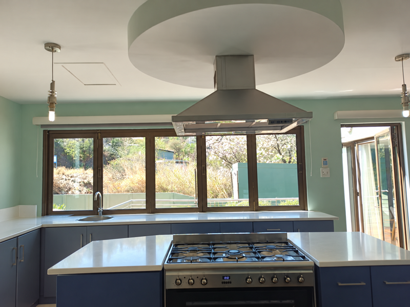 Modern kitchen featuring a central island with a gas cooktop, stainless steel extractor fan, stone countertops, and ample cabinetry with views to the exterior.