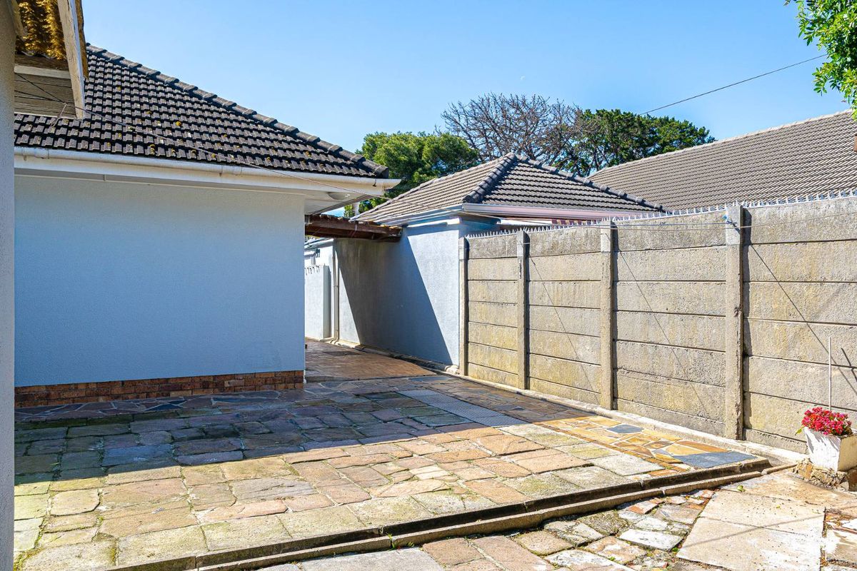 A rear exterior view showing a paved patio area, concrete boundary wall, and tiled roof sections of the property.