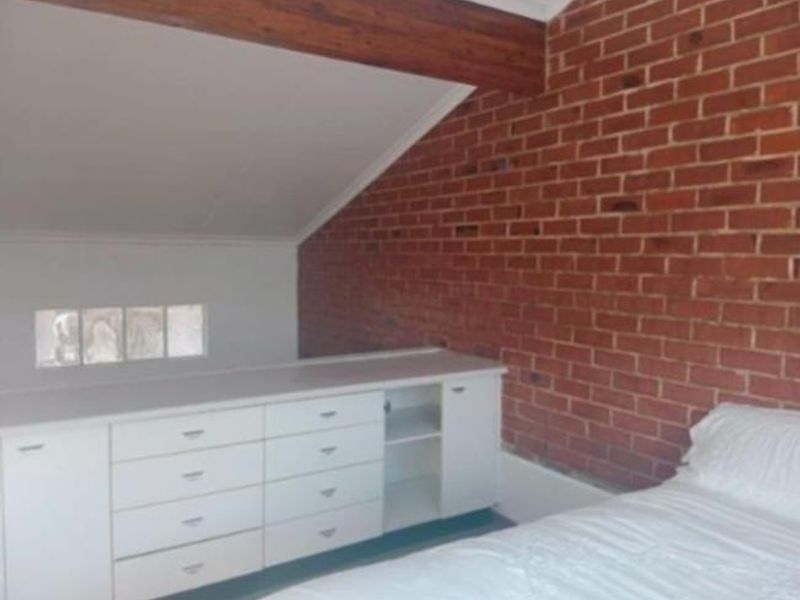 A bedroom featuring an exposed brick wall, sloped ceiling with a timber beam, and integrated built-in cabinetry for storage.