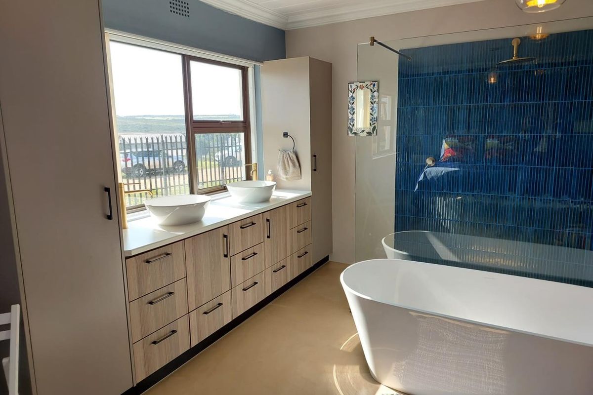 Modern bathroom featuring a double vanity with vessel sinks, a freestanding bathtub, and a stylish blue tiled walk-in shower with brass fixtures.