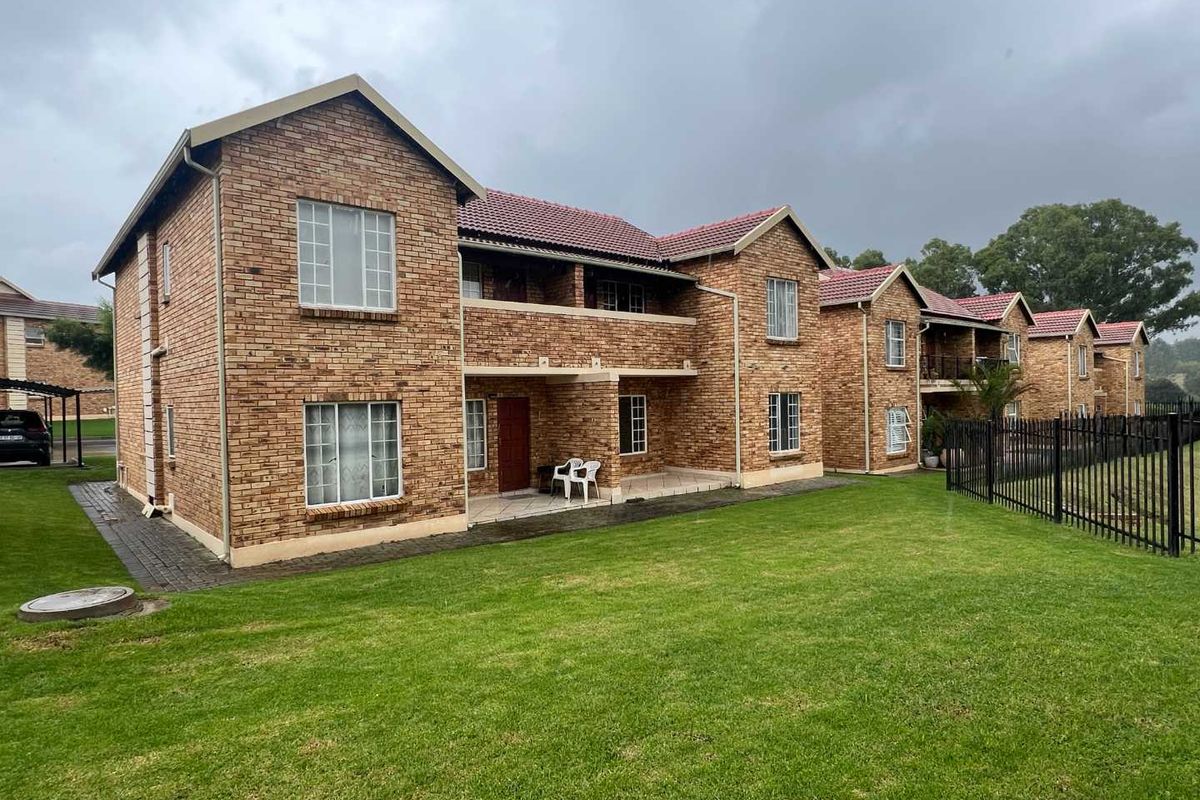 Exterior view of a multi-unit apartment complex featuring face-brick facades, tiled roofs, and ground-floor patio areas set within a well-maintained communal garden.