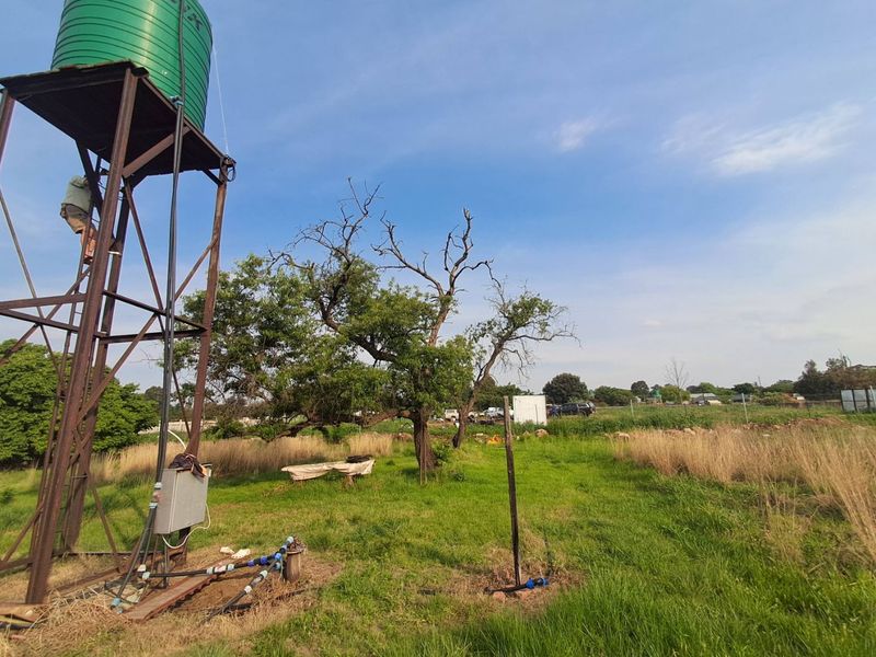 Outdoor area featuring a water storage tank on a steel stand and borehole infrastructure set within a grassy small holding landscape.