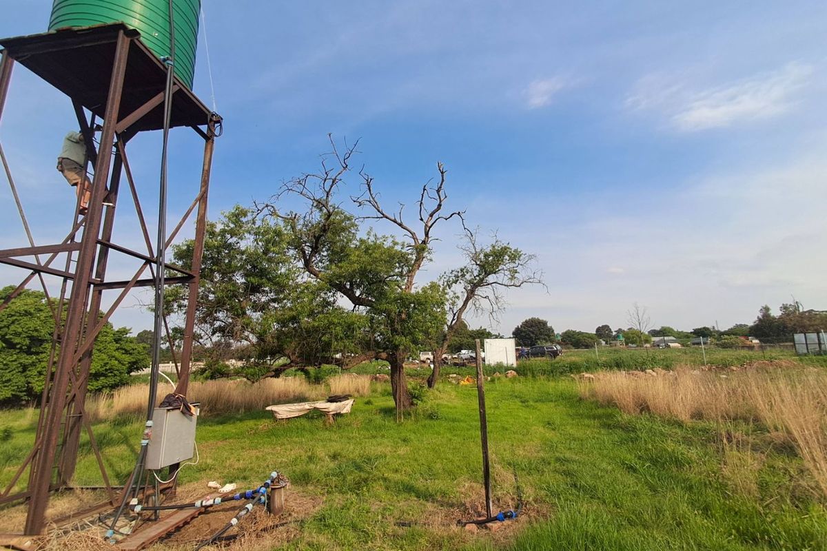 Outdoor area featuring a water storage tank on a steel stand and borehole infrastructure set within a grassy small holding landscape.