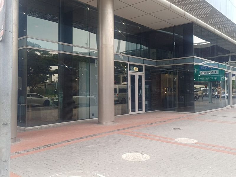 Modern retail storefront featuring extensive glass facade, steel structural columns, and a covered paved walkway entrance.