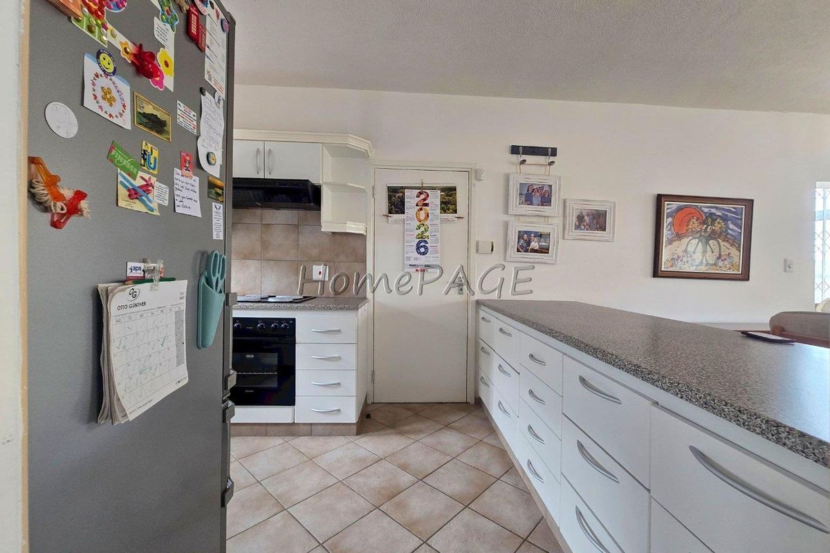 A functional kitchen featuring white cabinetry, granite-look countertops, a built-in oven with extractor fan, and tiled flooring.