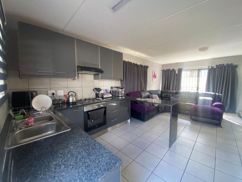Open-plan living area featuring a modern kitchen with dark cabinetry, granite countertops, built-in oven, gas hob, and a breakfast bar, flowing into the lounge.
