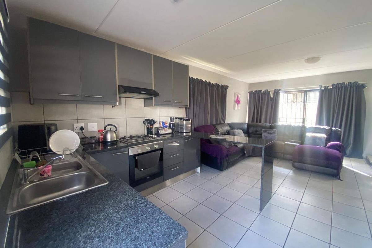 Open-plan living area featuring a modern kitchen with dark cabinetry, granite countertops, built-in oven, gas hob, and a breakfast bar, flowing into the lounge.