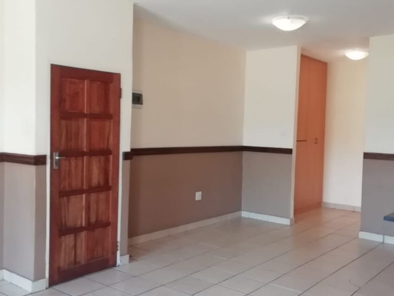 An empty open-plan living area featuring tiled floors, neutral wall paint with a dado rail, and built-in storage cupboards.