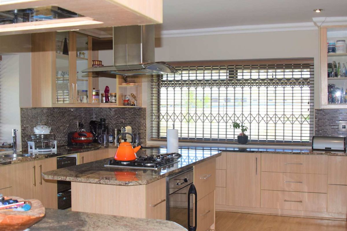 A well-appointed kitchen featuring light wood cabinetry, granite countertops, a central island with a built-in gas hob and oven, and a stainless steel extractor fan.