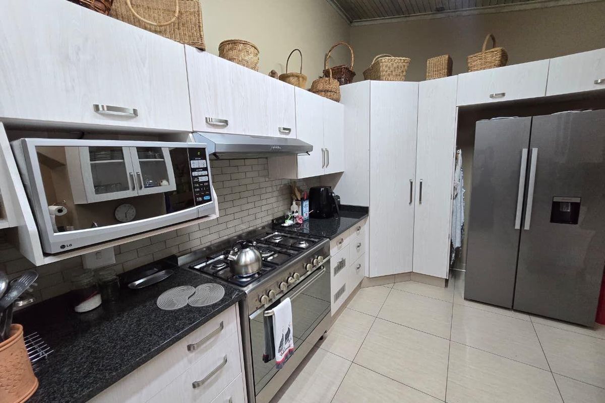A functional kitchen featuring light wood-grain cabinetry, dark granite countertops, a built-in gas hob, extractor fan, and tiled flooring.