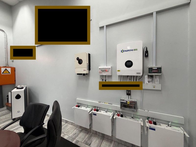 A clean utility space featuring a wall-mounted solar inverter and battery storage system with organized electrical conduit and distribution components.