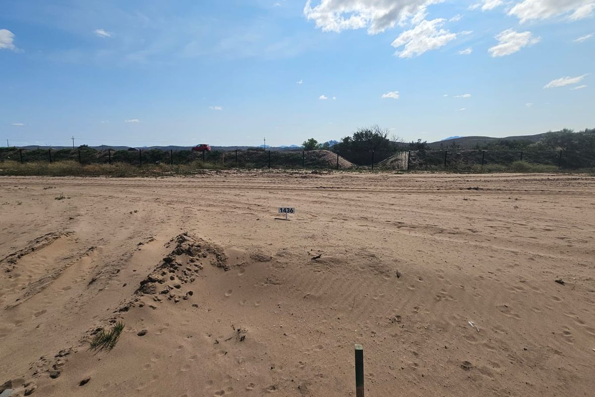 A vacant plot of land featuring sandy terrain, marked with a lot number, and enclosed by a perimeter fence.