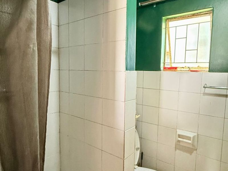 A functional bathroom featuring a shower enclosure, toilet, and tiled finishes, requiring cosmetic updates to improve its overall condition and aesthetic appeal.