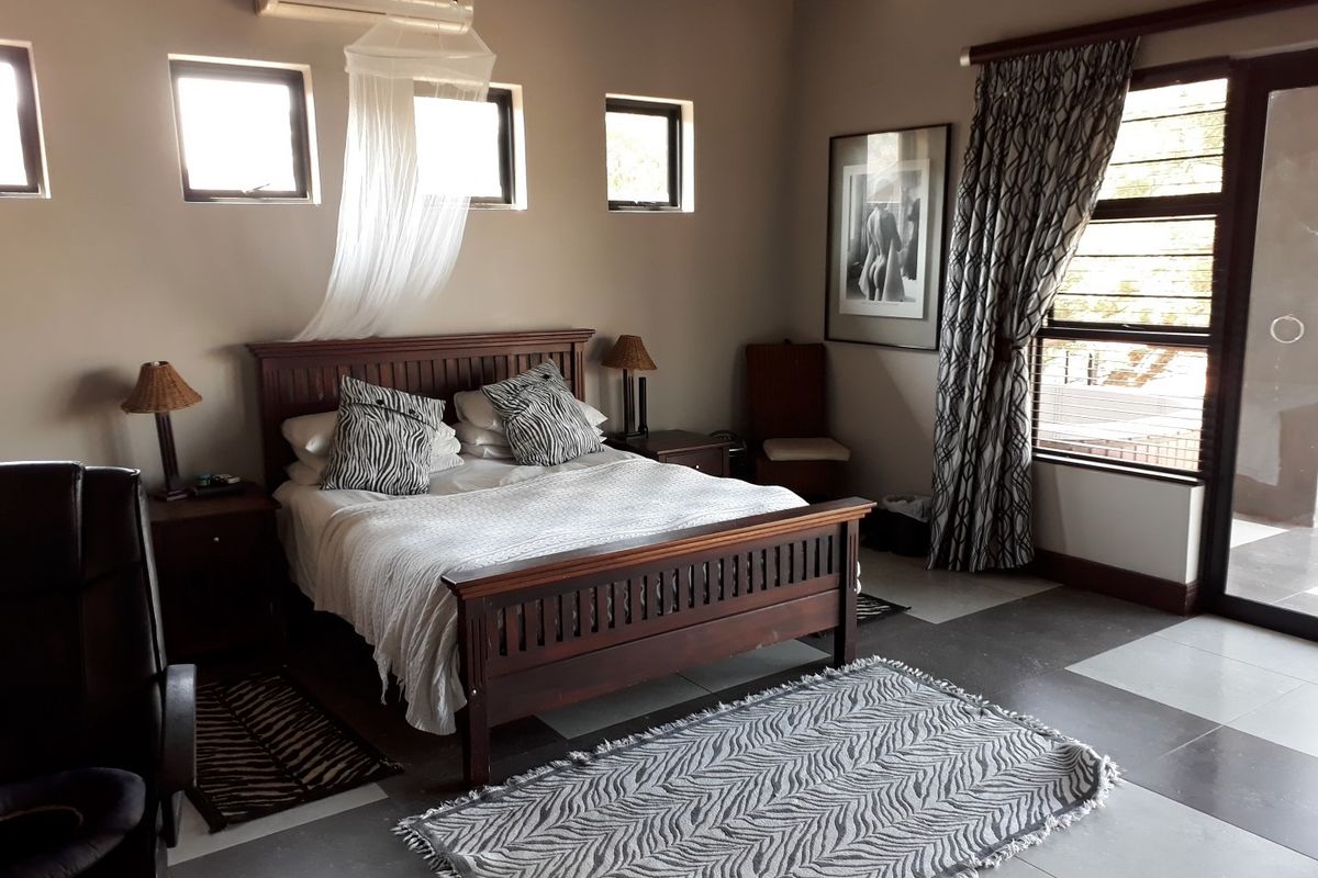 A well-maintained bedroom featuring tiled flooring, multiple windows for natural light, and a wall-mounted air conditioning unit.