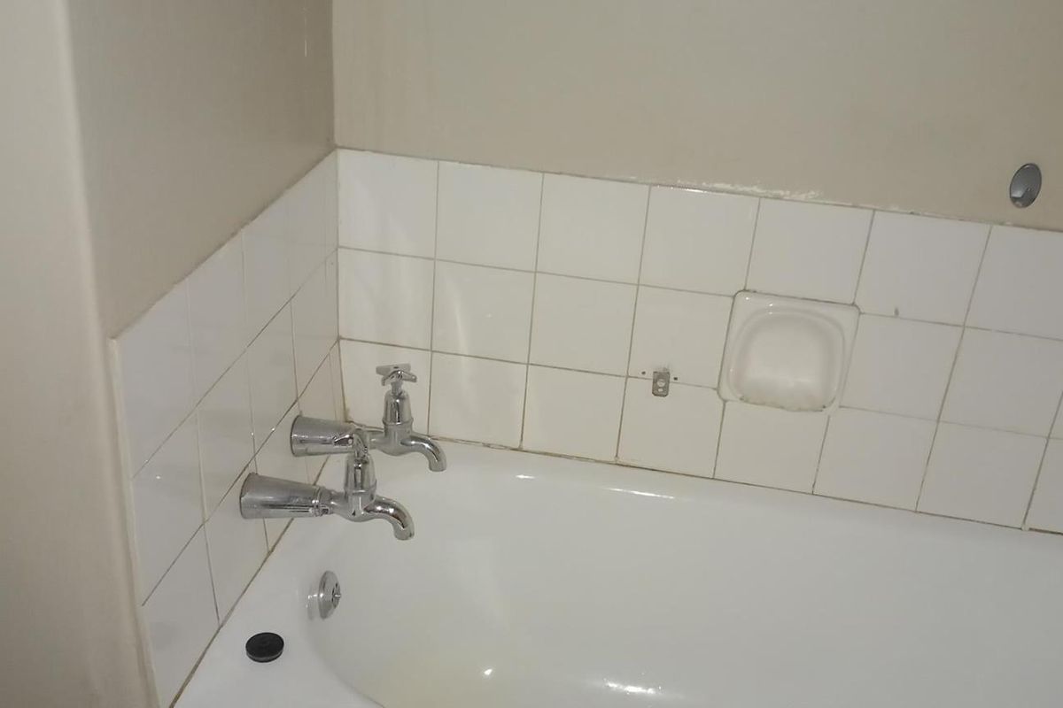 A basic bathroom featuring a standard bathtub with chrome faucets and white wall tiling, currently showing signs of wear and missing fixtures.