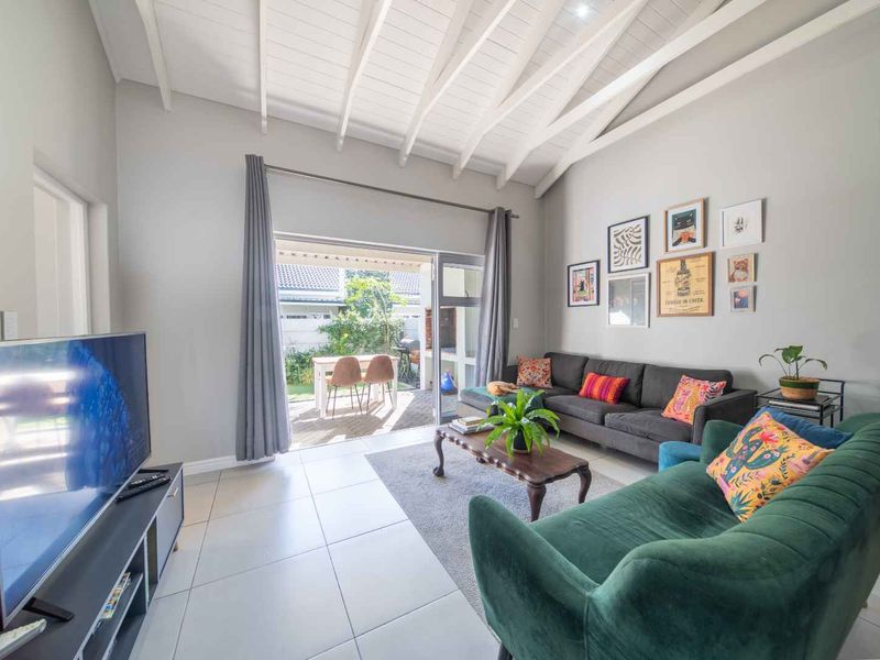 Bright living room featuring a high vaulted ceiling with exposed rafters, neutral tiled flooring, and large sliding glass doors opening to a private patio.