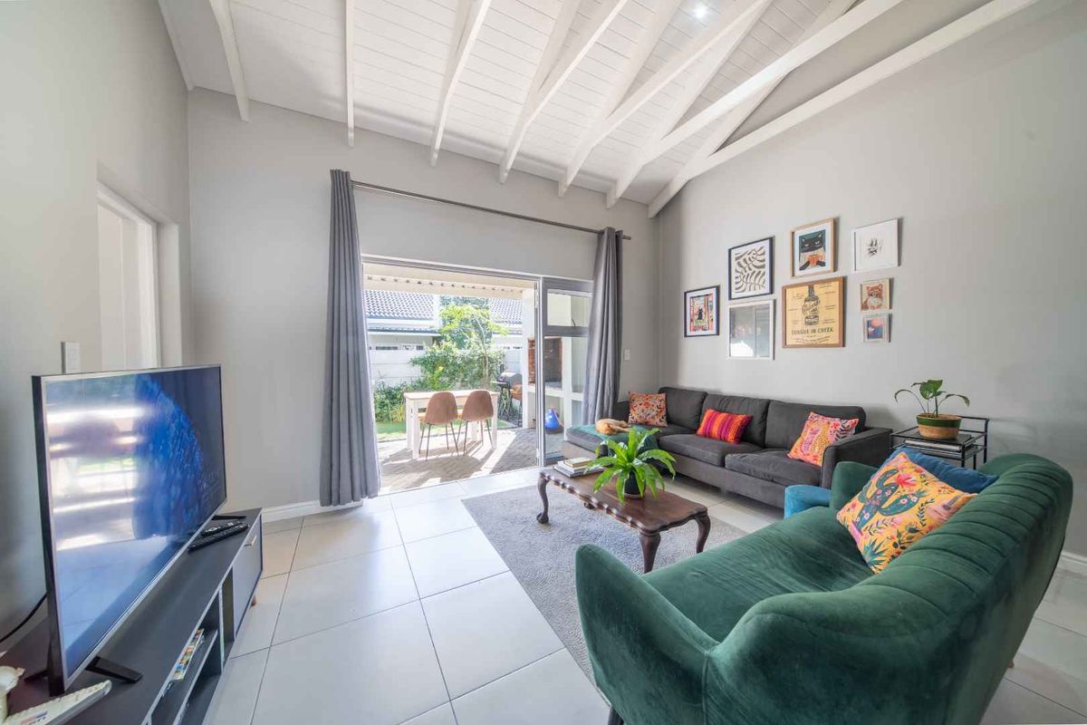 Bright living room featuring a high vaulted ceiling with exposed rafters, neutral tiled flooring, and large sliding glass doors opening to a private patio.