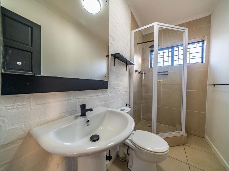 A clean and functional bathroom featuring a pedestal basin, a corner shower enclosure, and neutral wall and floor tiling.