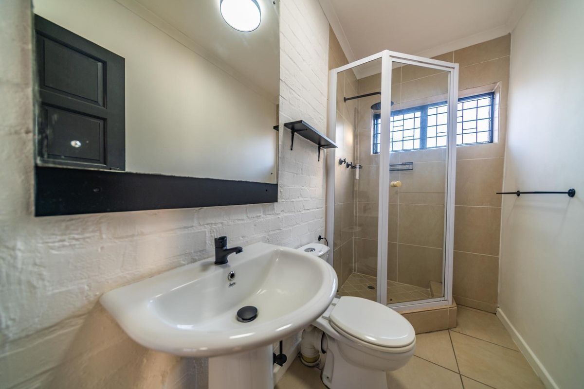 A clean and functional bathroom featuring a pedestal basin, a corner shower enclosure, and neutral wall and floor tiling.