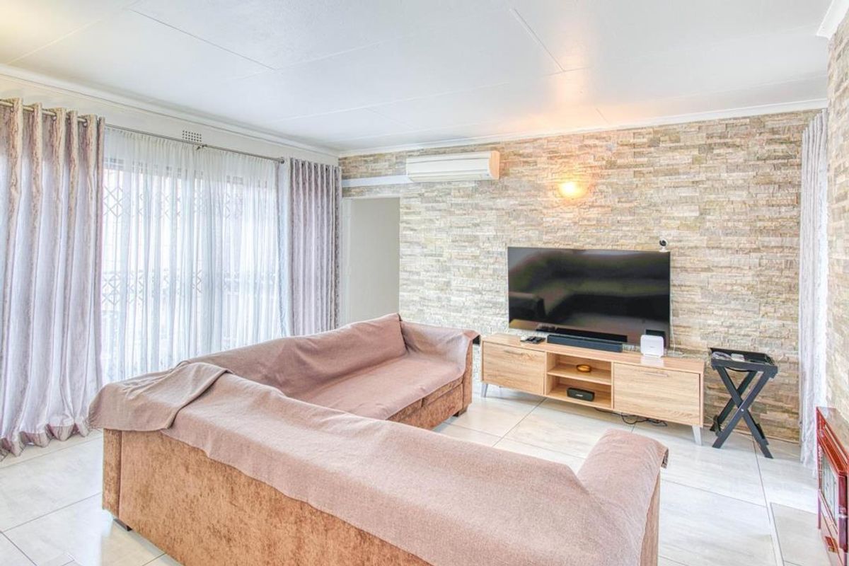 A comfortable living room featuring a textured stone feature wall, tiled flooring, and a wall-mounted air conditioning unit.
