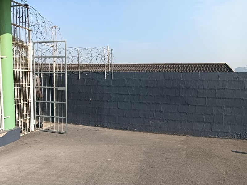 A secure exterior area featuring a painted concrete block boundary wall topped with razor wire and a metal security gate.
