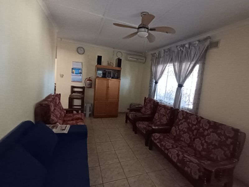 A living room featuring tiled flooring, a ceiling fan, and a wall-mounted air conditioning unit.