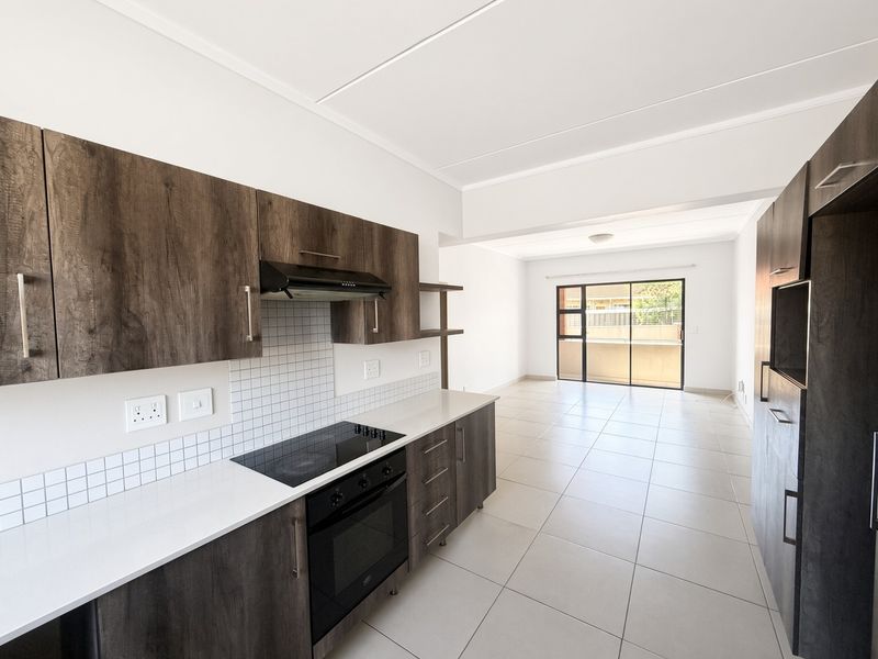 Modern open-plan kitchen and living area featuring dark wood cabinetry, integrated appliances, tiled flooring, and a sliding door leading to a balcony.