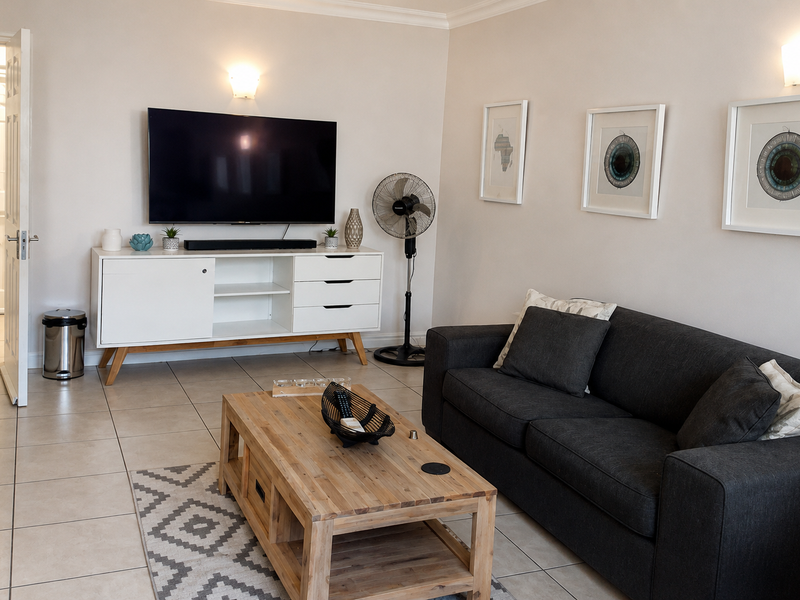 A well-maintained living room featuring neutral tiled flooring, coved ceilings, and wall-mounted lighting, providing a clean and functional space.
