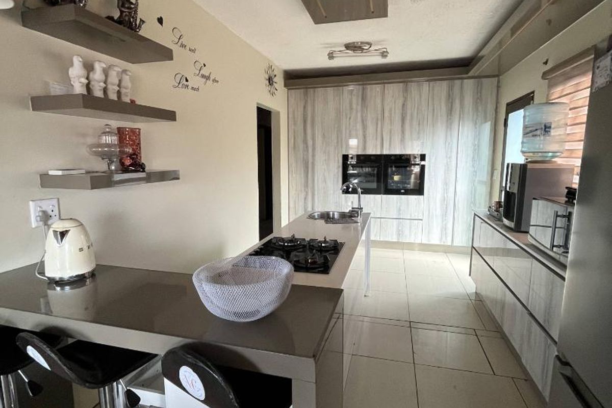 Modern kitchen featuring a central island with a gas hob, built-in double ovens, sleek cabinetry, and tiled flooring.