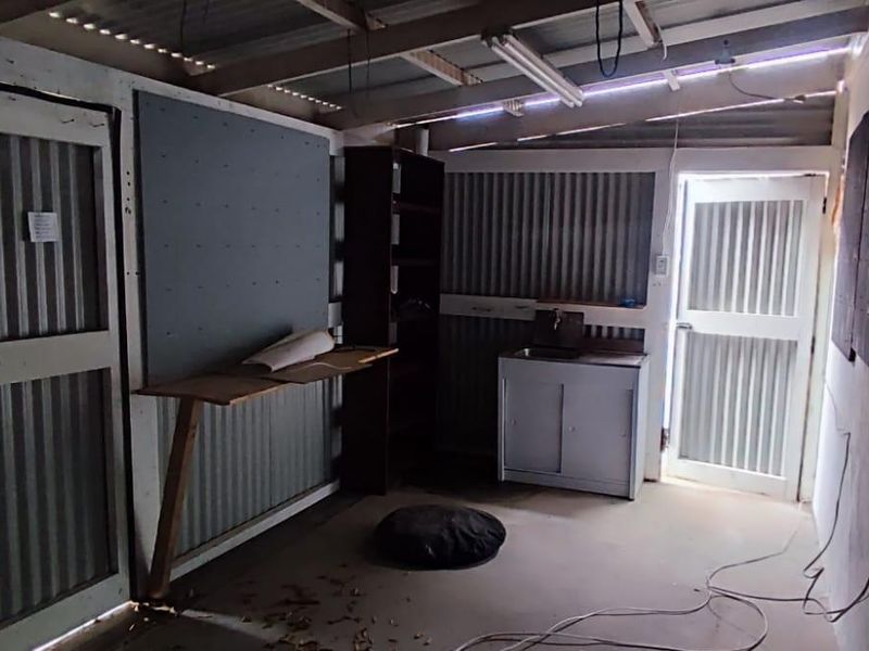 A functional utility space featuring corrugated metal walls, exposed rafters, and a basic sink unit, suitable for a workshop or storage area.