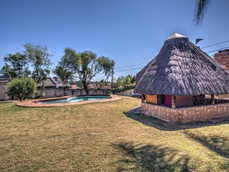 Spacious backyard featuring a swimming pool with brick surround and a traditional thatch lapa structure.