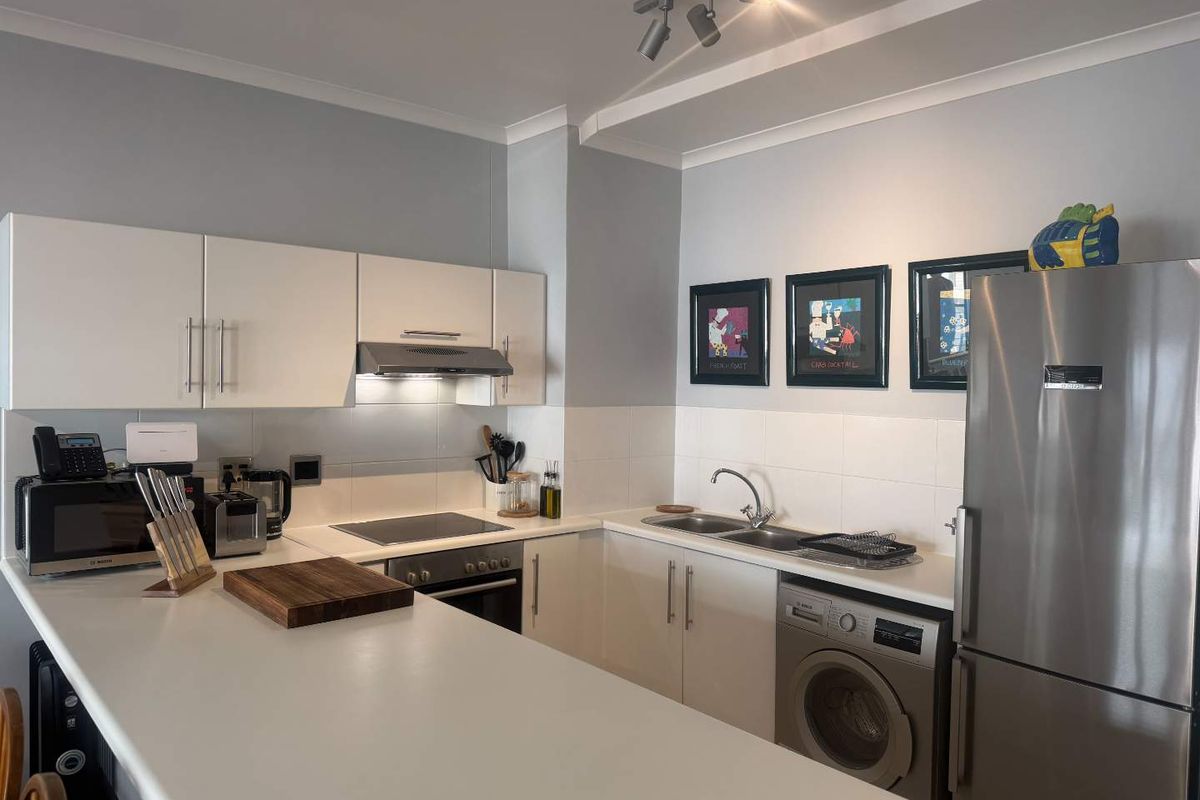 A functional kitchen featuring white cabinetry, a built-in oven, electric hob, extractor fan, double sink, and integrated laundry appliance space.