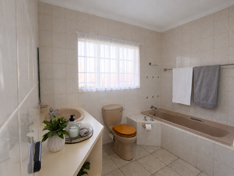 A functional bathroom featuring a built-in vanity with inset basin, a toilet, and a tiled bathtub surround with neutral wall and floor tiling.