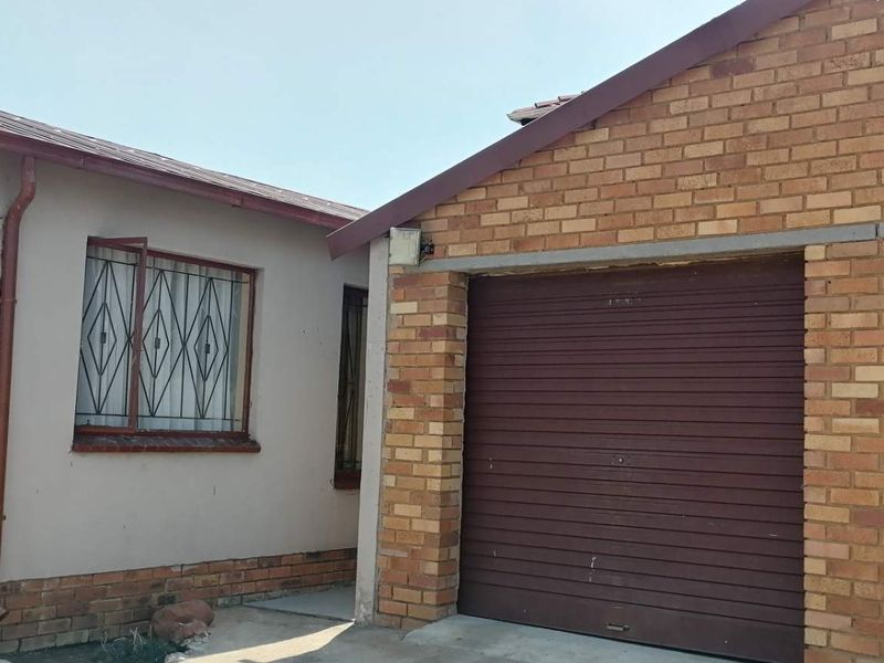 Front exterior view of the property featuring a double garage with roller doors and an adjacent plastered wall with security-barred windows.