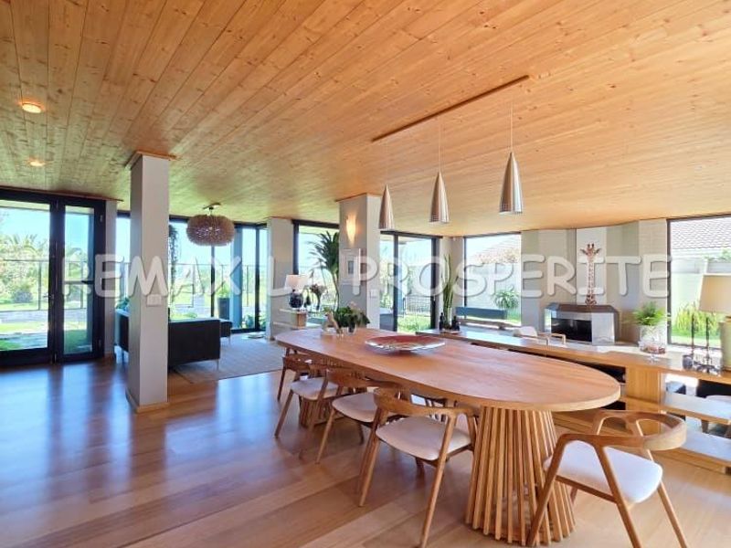 Spacious open-plan living and dining area featuring warm timber ceilings, hardwood flooring, a fireplace, and extensive glass doors providing natural light and garden views.