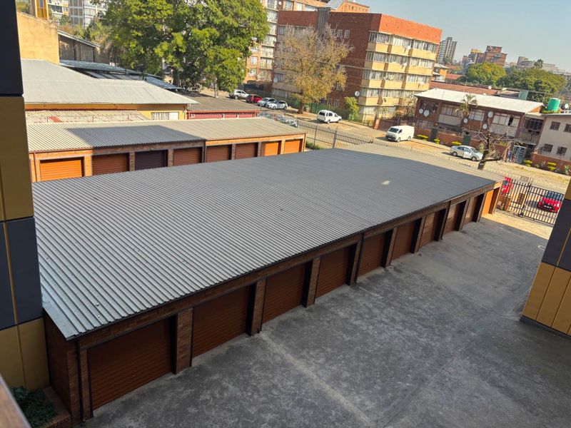 An elevated view of a row of brick garages featuring corrugated metal roofing and multiple roller shutter doors with a concrete driveway.