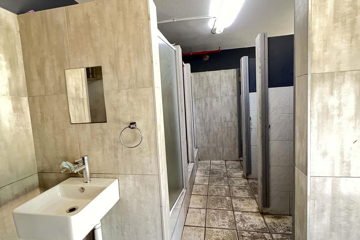 Industrial-style communal bathroom facility featuring multiple shower stalls, tiled wall finishes, and a wall-mounted basin.