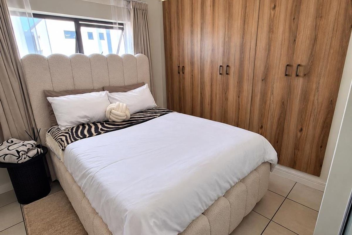 A well-maintained bedroom featuring modern wood-finish built-in cupboards, neutral tiled flooring, and a contemporary pendant light fixture.
