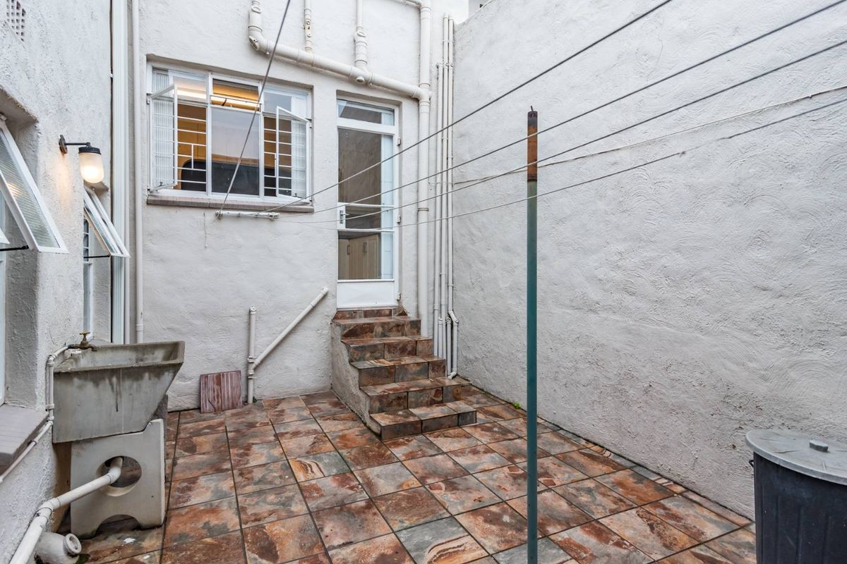 A functional rear courtyard area featuring tiled flooring, a concrete wash basin, and direct access to the interior via a small set of steps.