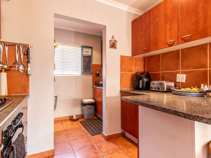 A functional kitchen featuring wooden cabinetry, granite countertops, tiled backsplash, and a built-in hob and oven, with an adjacent scullery area.