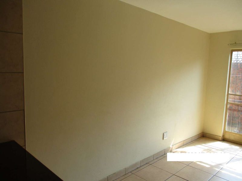 An empty living area featuring neutral tiled flooring and a sliding glass door providing natural light and access to the exterior.