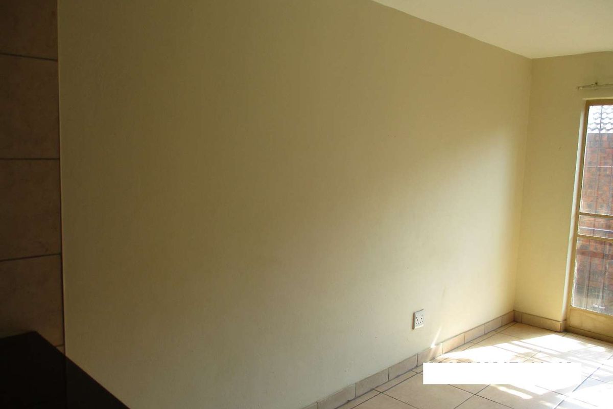 An empty living area featuring neutral tiled flooring and a sliding glass door providing natural light and access to the exterior.