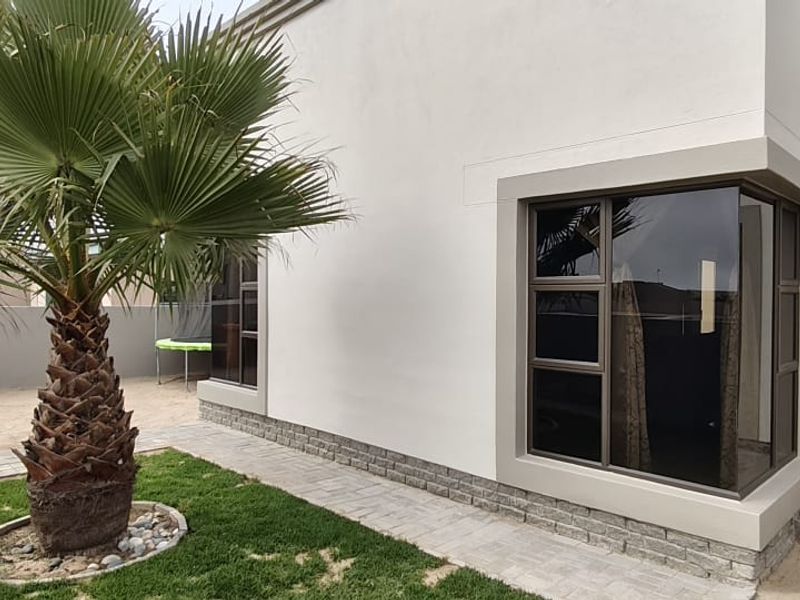 Rear exterior view of the property featuring modern stone cladding, large aluminium-framed windows, and a neatly paved garden walkway.