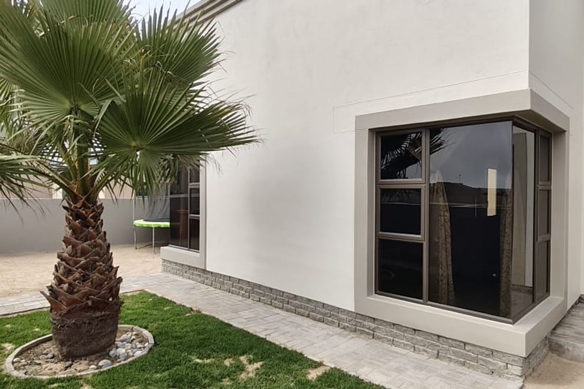 Rear exterior view of the property featuring modern stone cladding, large aluminium-framed windows, and a neatly paved garden walkway.
