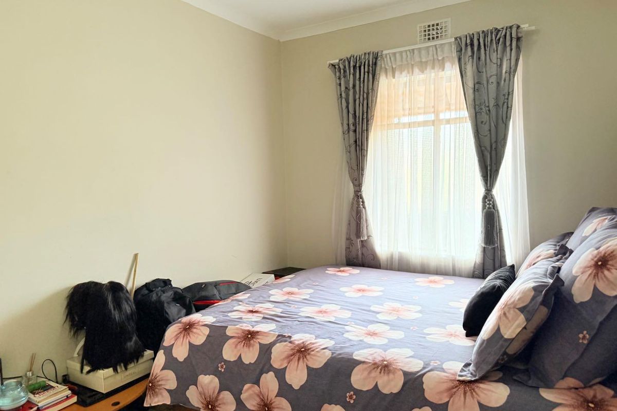 A standard bedroom featuring neutral wall finishes, a window with curtain tracks, and a ceiling ventilation vent.
