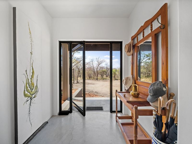 Bright entrance hall featuring polished concrete flooring and a modern black-framed glass pivot door opening to the exterior.