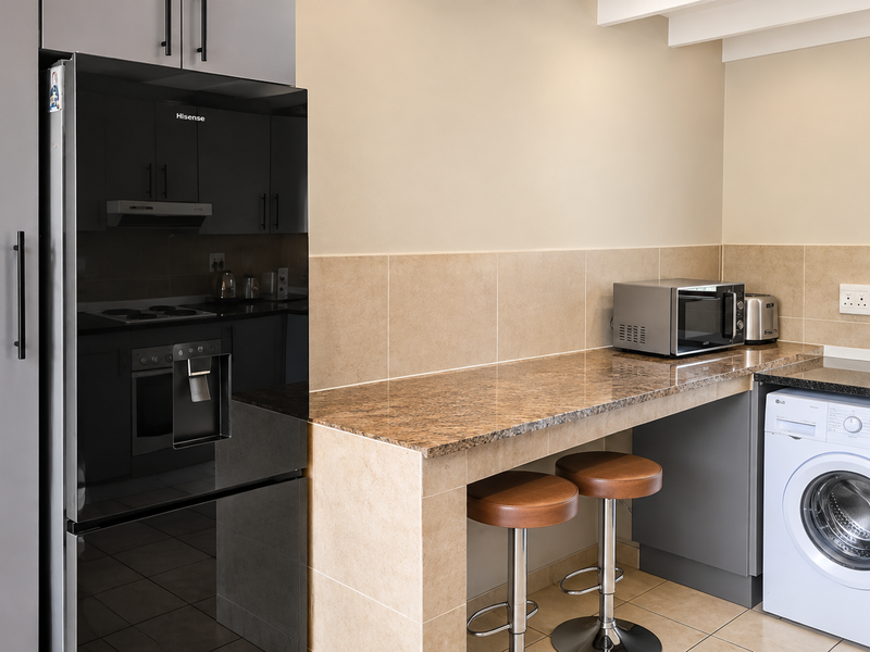 Modern kitchen featuring granite countertops, tiled backsplash, built-in cabinetry, integrated washing machine, and a breakfast bar area.